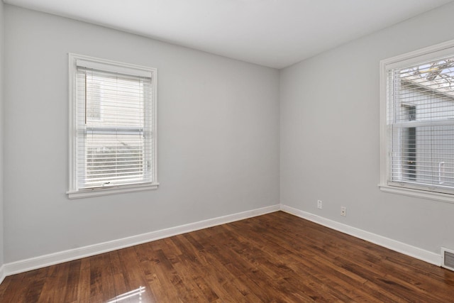 unfurnished room featuring dark wood-type flooring, visible vents, and baseboards