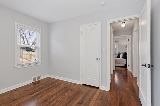 unfurnished bedroom featuring baseboards, visible vents, and dark wood-style flooring