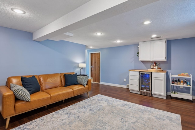 living room featuring dark wood-type flooring, baseboards, wine cooler, a textured ceiling, and a bar