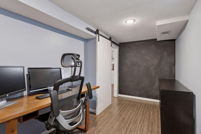 office space with wood finished floors, baseboards, visible vents, a textured ceiling, and a barn door