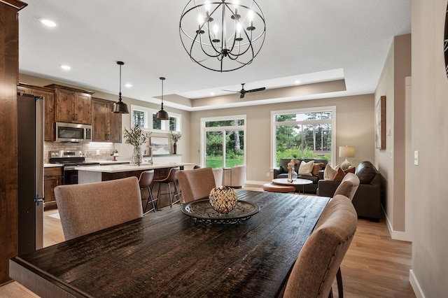 dining room with a raised ceiling, sink, ceiling fan with notable chandelier, and light hardwood / wood-style flooring