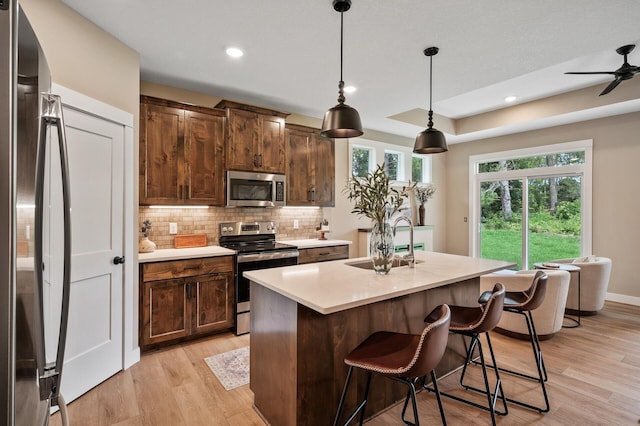 kitchen with appliances with stainless steel finishes, pendant lighting, an island with sink, backsplash, and light wood-type flooring