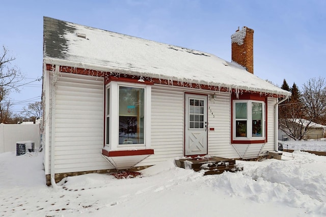 snow covered back of property featuring a chimney and fence