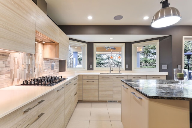 kitchen with light tile patterned floors, stainless steel gas stovetop, a sink, and light brown cabinetry