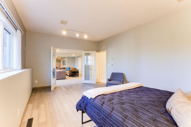 bedroom with french doors, light wood finished floors, visible vents, track lighting, and baseboards