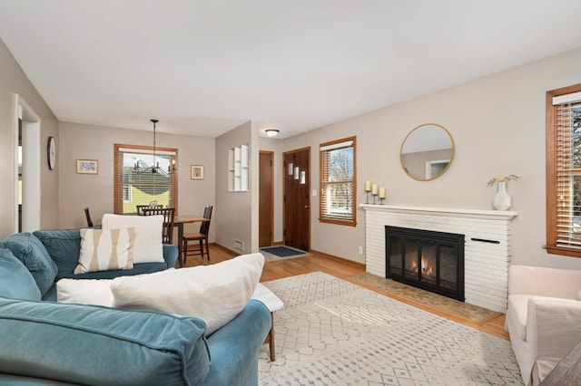 living area featuring baseboards, light wood finished floors, a fireplace, and an inviting chandelier