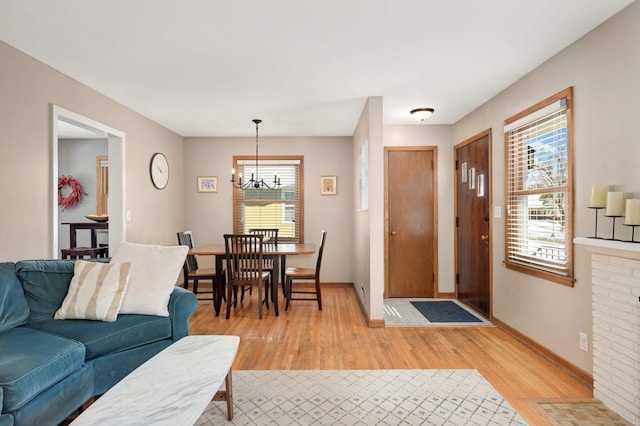 living area featuring light wood-style floors, a notable chandelier, and baseboards