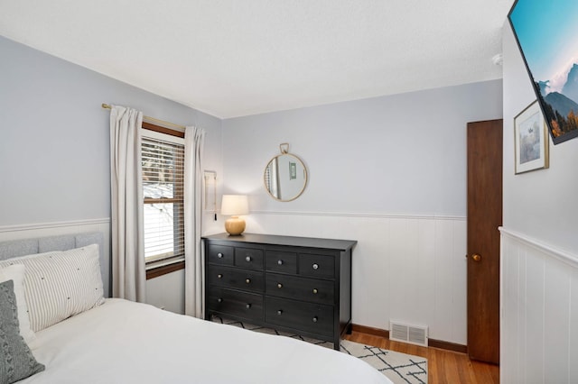 bedroom featuring visible vents, wood finished floors, and wainscoting