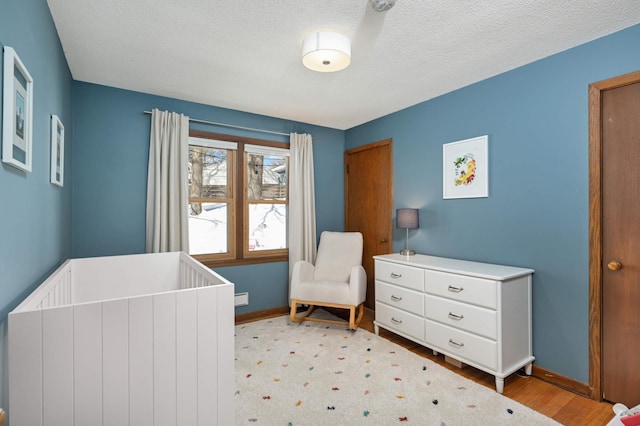 bedroom with a nursery area, a textured ceiling, baseboards, and wood finished floors