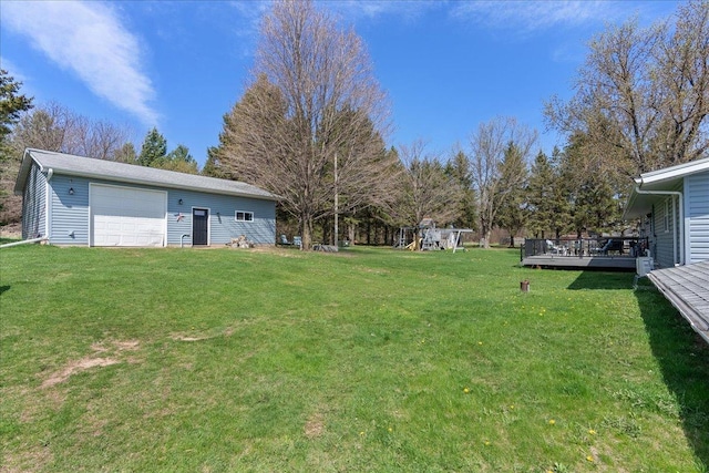 view of yard with a detached garage, an outbuilding, a wooden deck, and a playground
