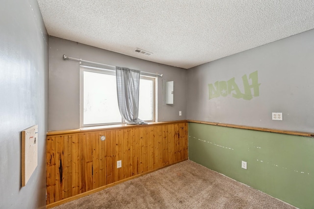 carpeted empty room with a textured ceiling and wooden walls