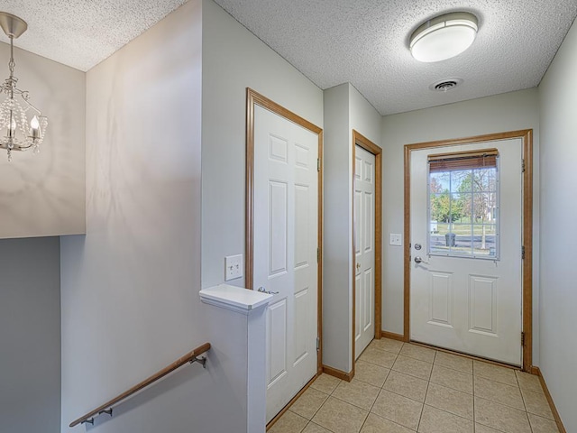 entryway with a notable chandelier, a textured ceiling, and light tile patterned floors