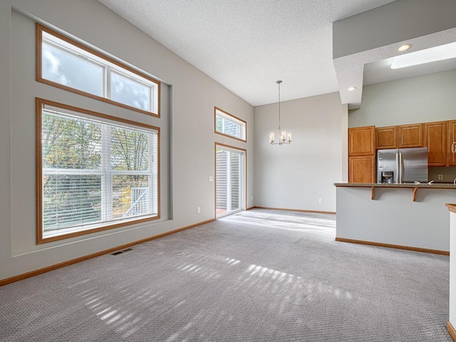 unfurnished living room featuring a towering ceiling, a chandelier, light carpet, and a textured ceiling