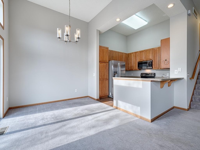 kitchen with hanging light fixtures, a kitchen breakfast bar, stainless steel appliances, light colored carpet, and kitchen peninsula