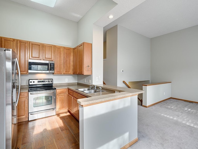 kitchen with sink, stainless steel appliances, a textured ceiling, kitchen peninsula, and light wood-type flooring