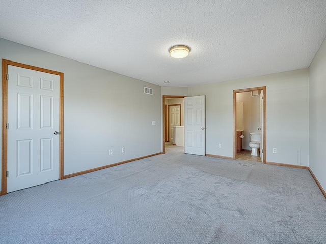 unfurnished bedroom featuring light colored carpet, ensuite bathroom, and a textured ceiling