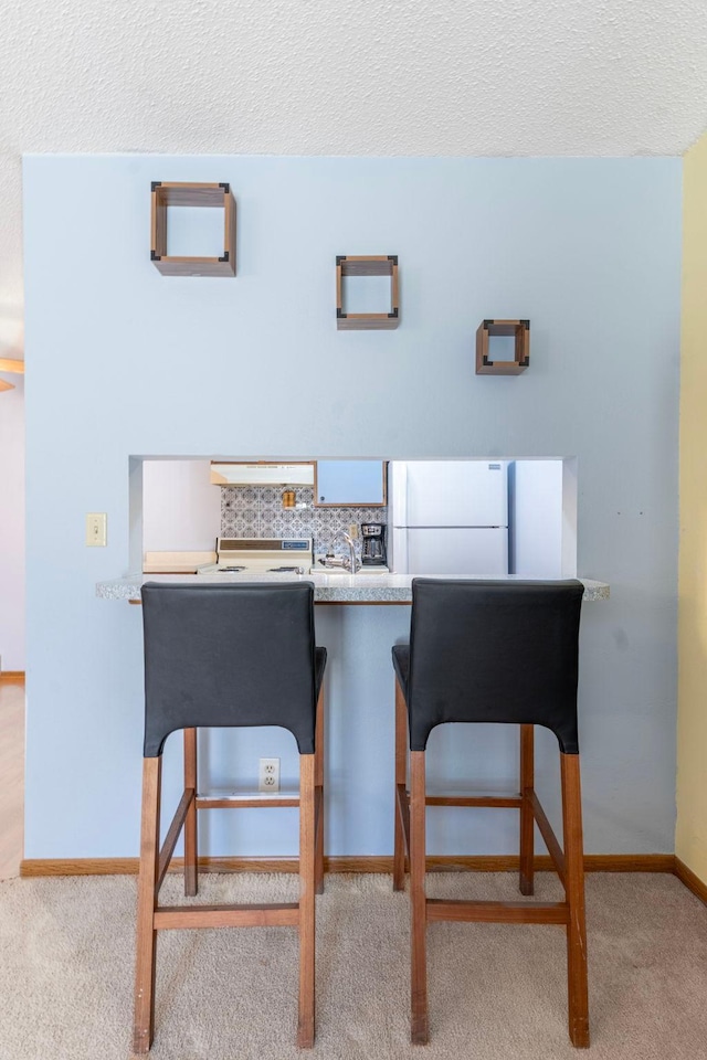 interior space with a textured ceiling, backsplash, carpet, and freestanding refrigerator