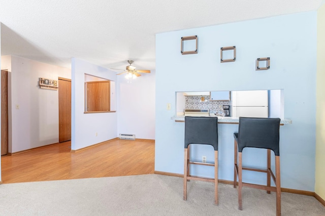 kitchen with tasteful backsplash, a breakfast bar, freestanding refrigerator, wood finished floors, and a ceiling fan