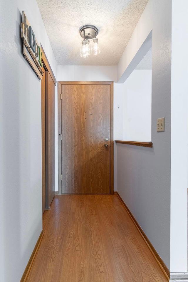 hall featuring wood finished floors, baseboards, and a textured ceiling