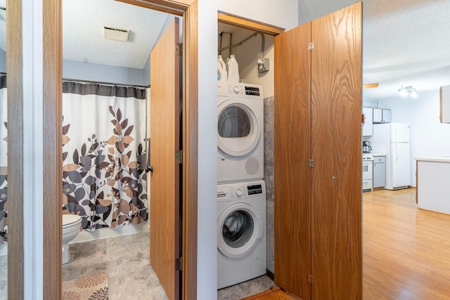 laundry room featuring stacked washer / drying machine, a textured ceiling, light wood-style flooring, and laundry area