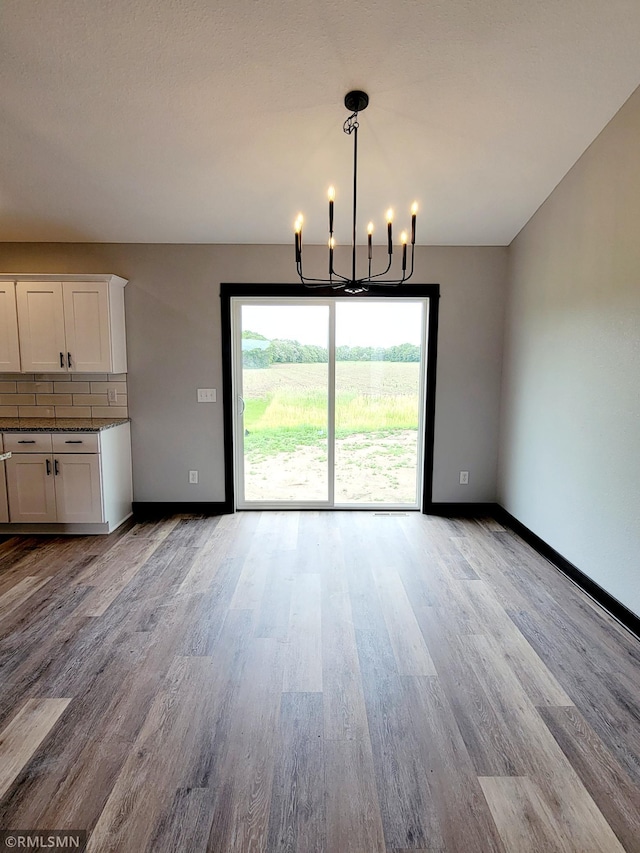 unfurnished dining area featuring an inviting chandelier and light hardwood / wood-style flooring