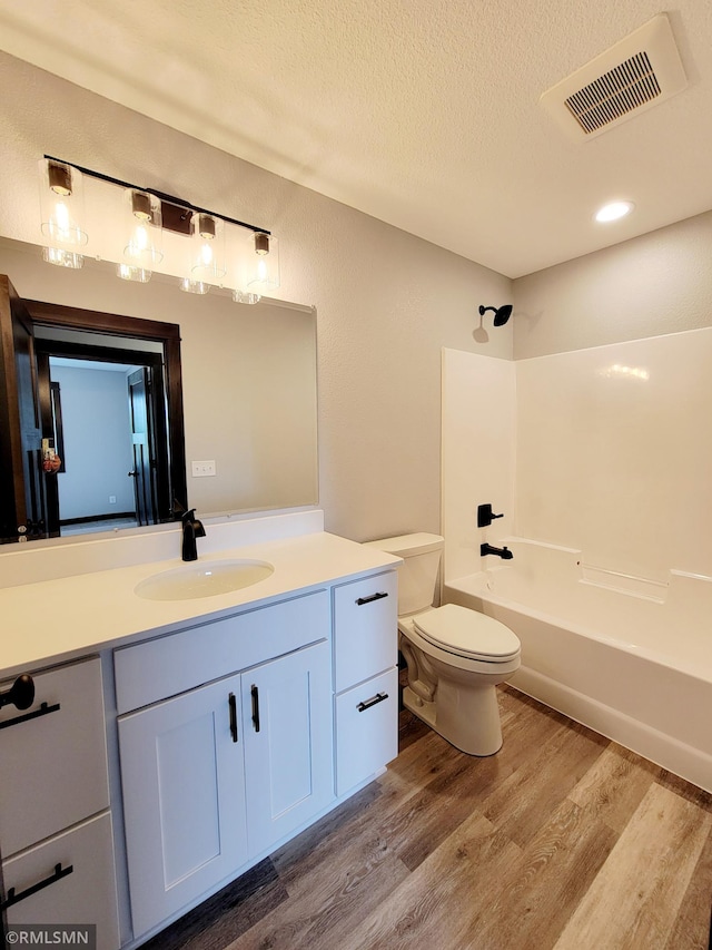 full bathroom with hardwood / wood-style flooring, bathing tub / shower combination, vanity, a textured ceiling, and toilet