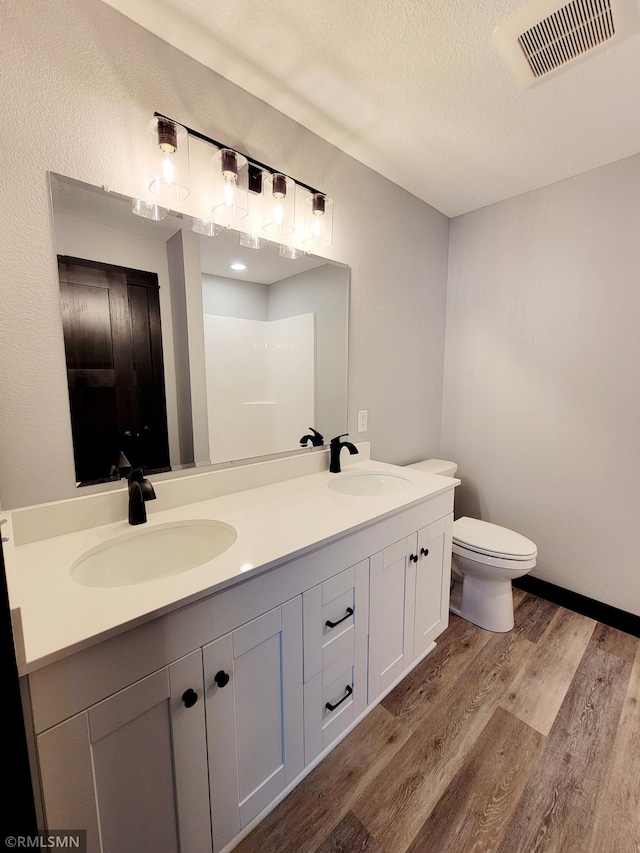 bathroom with hardwood / wood-style floors, vanity, walk in shower, toilet, and a textured ceiling