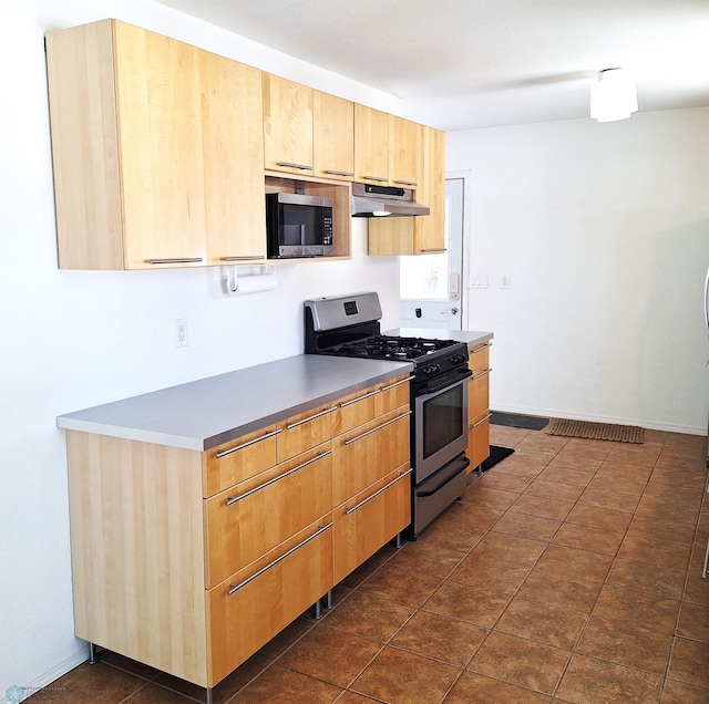 kitchen featuring light brown cabinetry, appliances with stainless steel finishes, under cabinet range hood, dark tile patterned floors, and baseboards