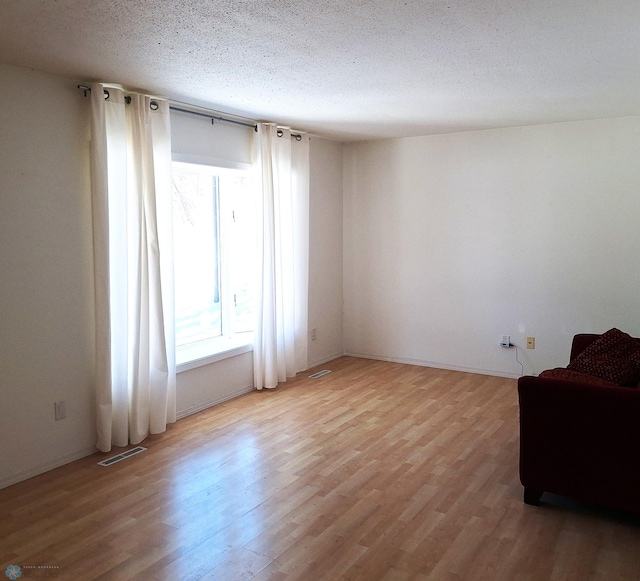 unfurnished room with a textured ceiling, light wood finished floors, and visible vents