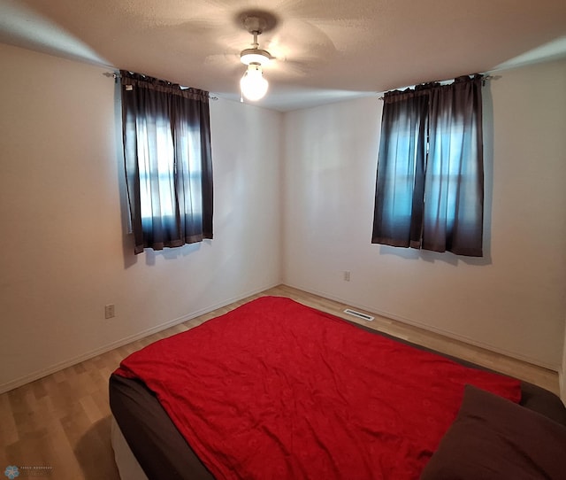 bedroom with visible vents, baseboards, ceiling fan, a textured ceiling, and light wood-style floors