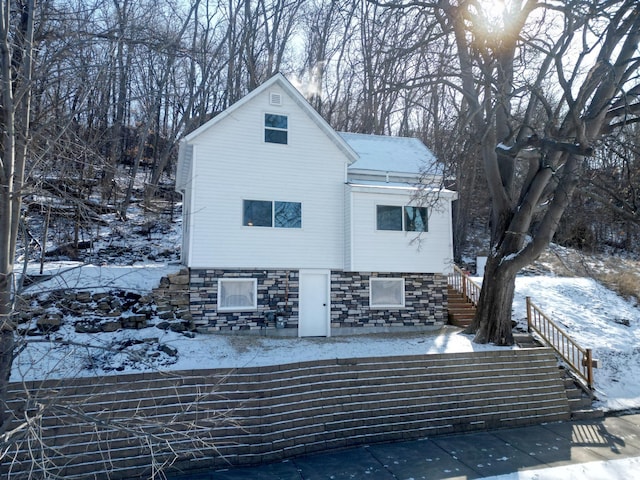 view of snow covered exterior with stone siding and stairway