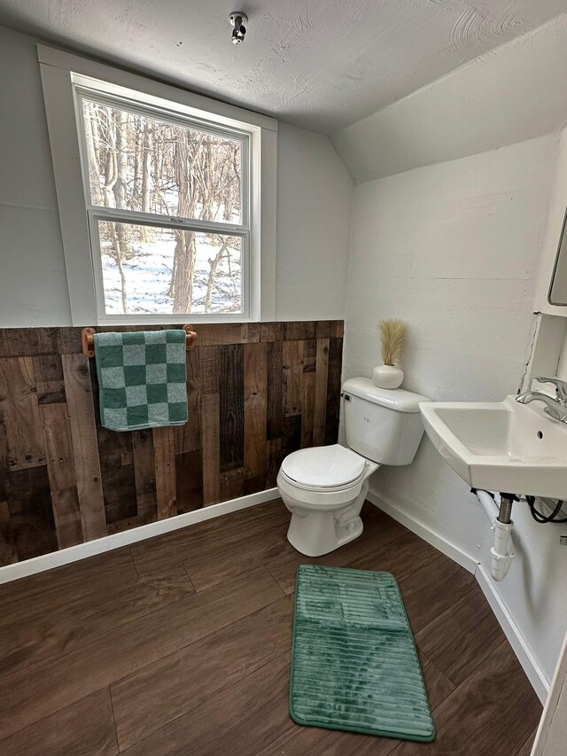 half bath featuring wooden walls, toilet, wood finished floors, vaulted ceiling, and a textured ceiling