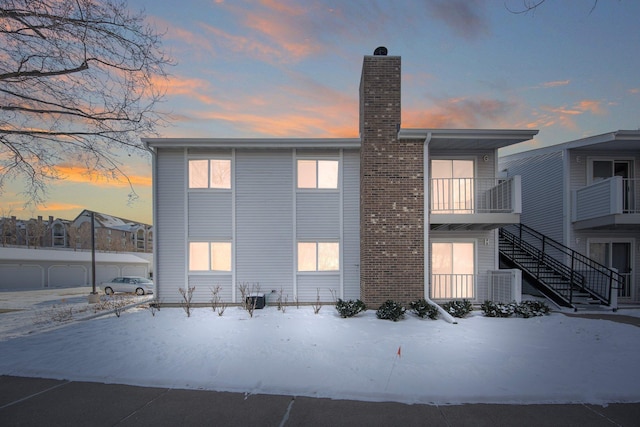 snow covered property with stairway and a chimney