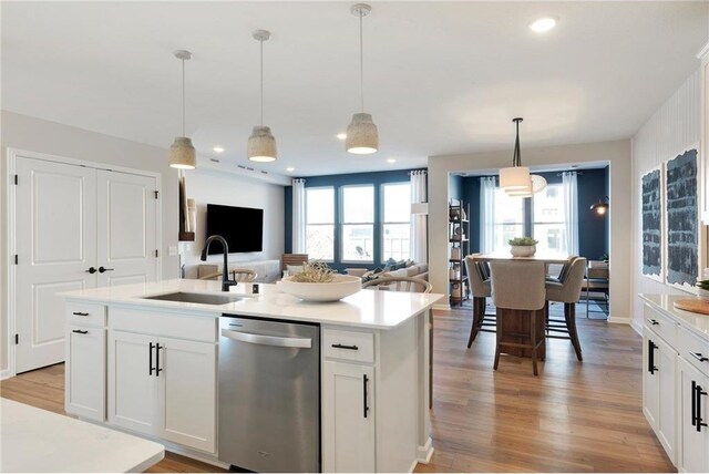kitchen featuring a center island with sink, light countertops, a sink, light wood-style flooring, and dishwasher