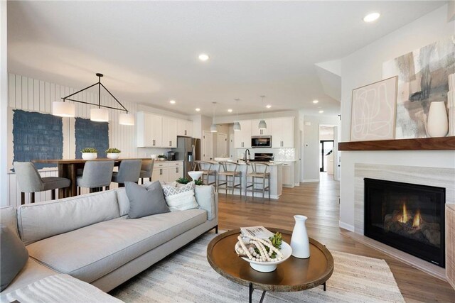 living area featuring recessed lighting, a warm lit fireplace, and light wood-style flooring
