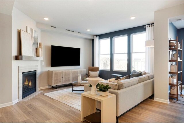 living area with a glass covered fireplace, light wood-style flooring, recessed lighting, baseboards, and visible vents