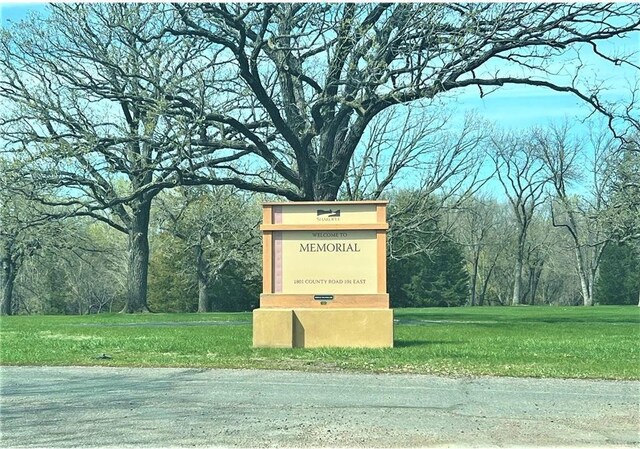 community sign featuring a lawn and a wooded view