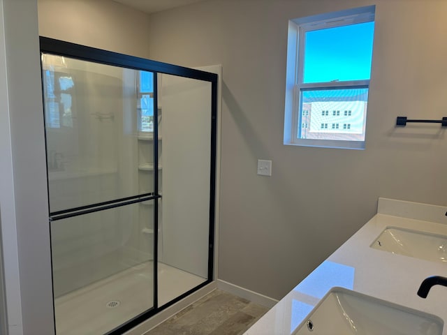 full bath with a sink, baseboards, a shower stall, and double vanity