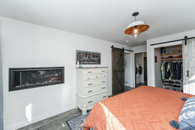 bedroom with washing machine and dryer, a barn door, baseboards, two closets, and dark wood-type flooring