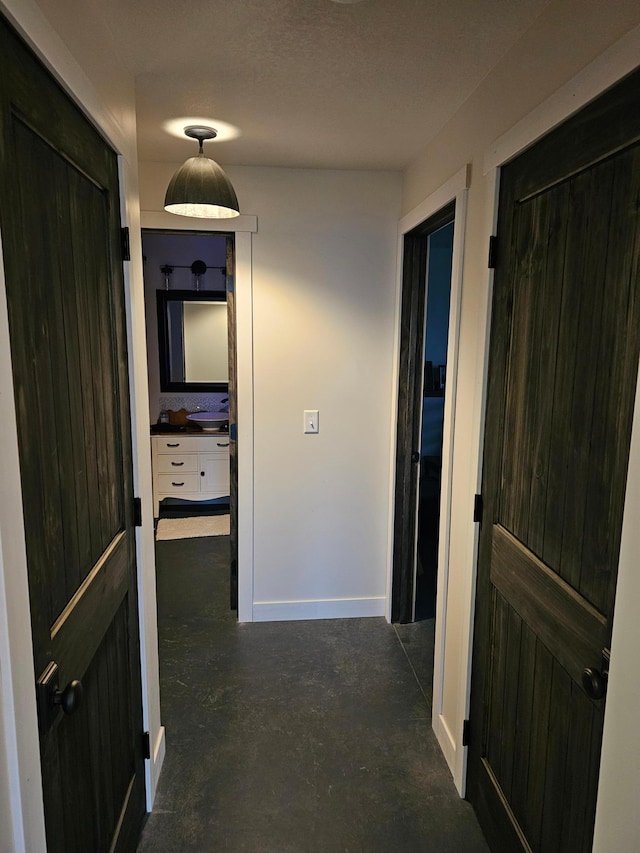 hallway featuring baseboards, a sink, and concrete flooring