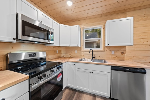 kitchen with white cabinetry, stainless steel appliances, wooden walls, and sink