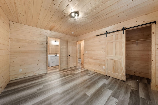 unfurnished bedroom with hardwood / wood-style flooring, ensuite bath, wooden ceiling, a barn door, and wood walls