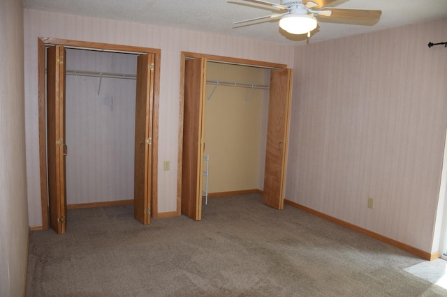 unfurnished bedroom featuring light carpet, ceiling fan, two closets, and a textured ceiling