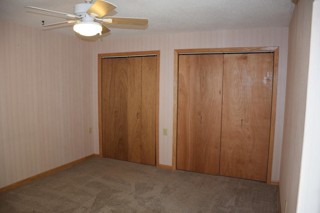 unfurnished bedroom featuring ceiling fan, a textured ceiling, light colored carpet, and multiple closets