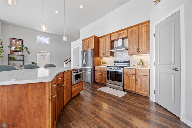 kitchen featuring tasteful backsplash, hanging light fixtures, stainless steel appliances, light stone countertops, and wall chimney range hood