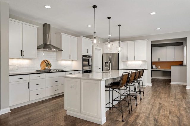 kitchen with a center island with sink, white cabinetry, appliances with stainless steel finishes, and wall chimney range hood