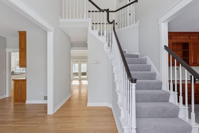 stairway with a high ceiling, wood finished floors, visible vents, and baseboards