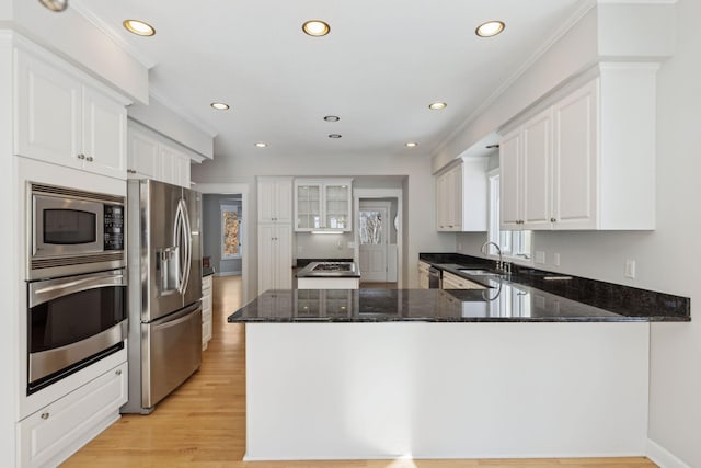 kitchen featuring dark stone counters, a peninsula, appliances with stainless steel finishes, and white cabinetry