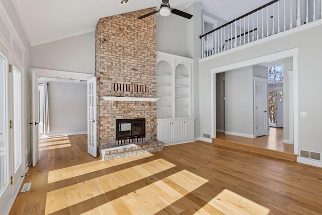 unfurnished living room featuring visible vents, baseboards, built in features, a brick fireplace, and wood-type flooring