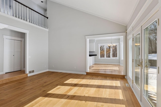 spare room featuring a notable chandelier, wood-type flooring, visible vents, high vaulted ceiling, and baseboards